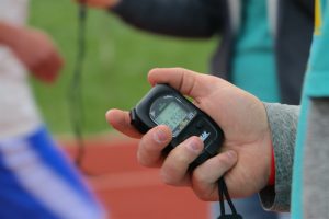 Human hand holding stopwatch at high school track and field event.