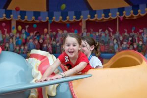 A young girl excited to be on the dumbo ride at Disney world amusement park.